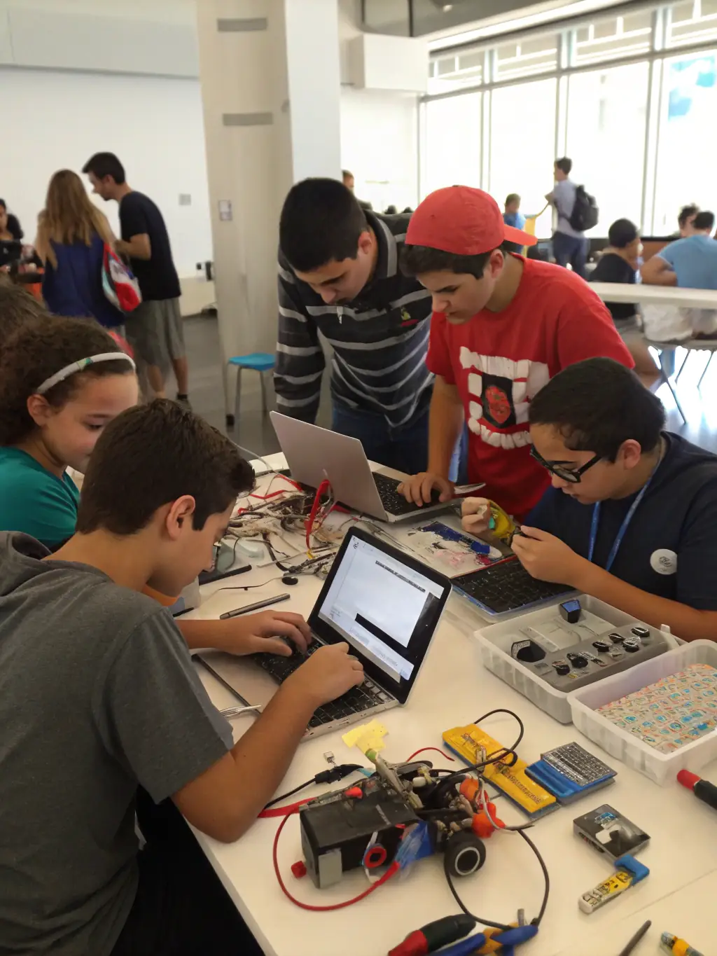 A group of young girls enthusiastically participating in a coding workshop, surrounded by laptops and colorful wires, showcasing the fun and engaging nature of GeekGirls' technology programs.
