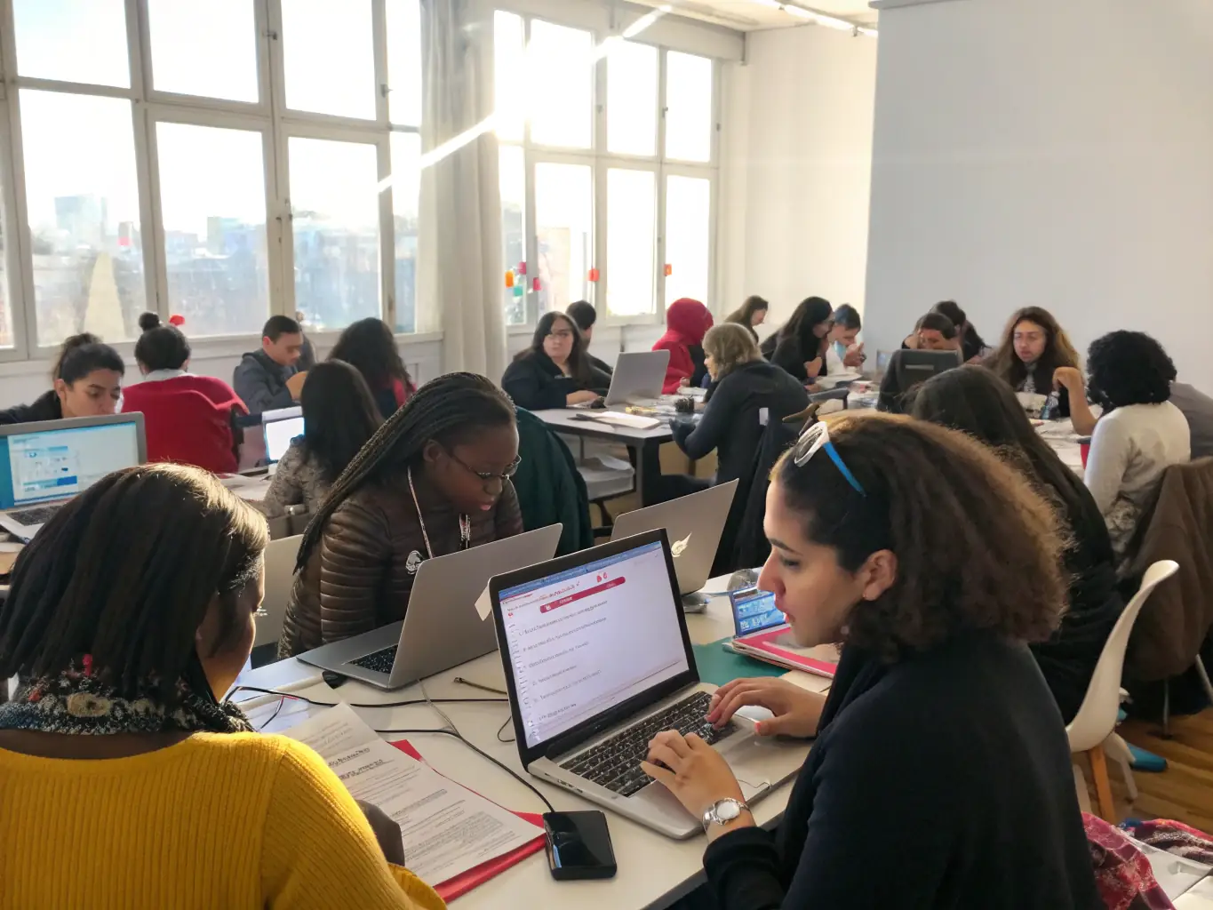 A diverse group of young participants engaged in a coding workshop, collaborating and learning together, surrounded by laptops and coding materials.